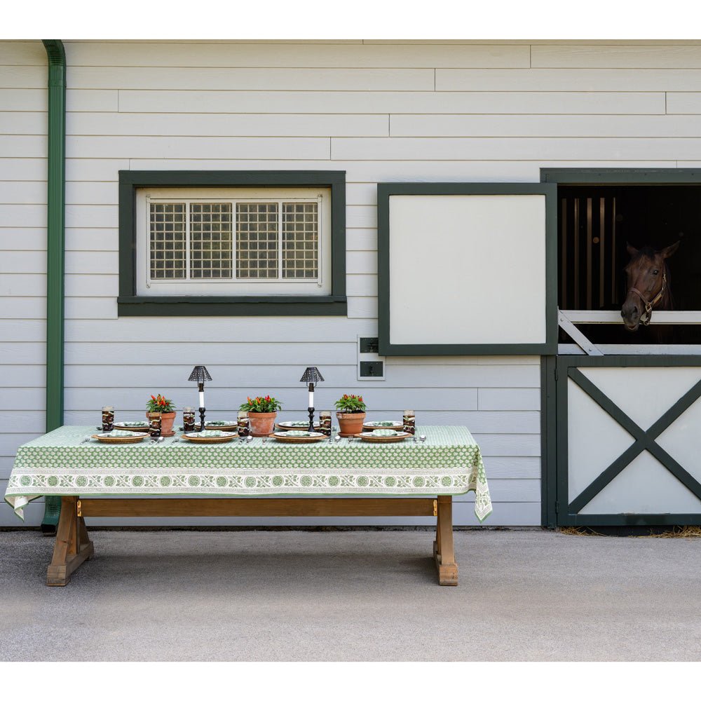 Table with pom buti green tablecloth in front of barn with horse peaking out of stall