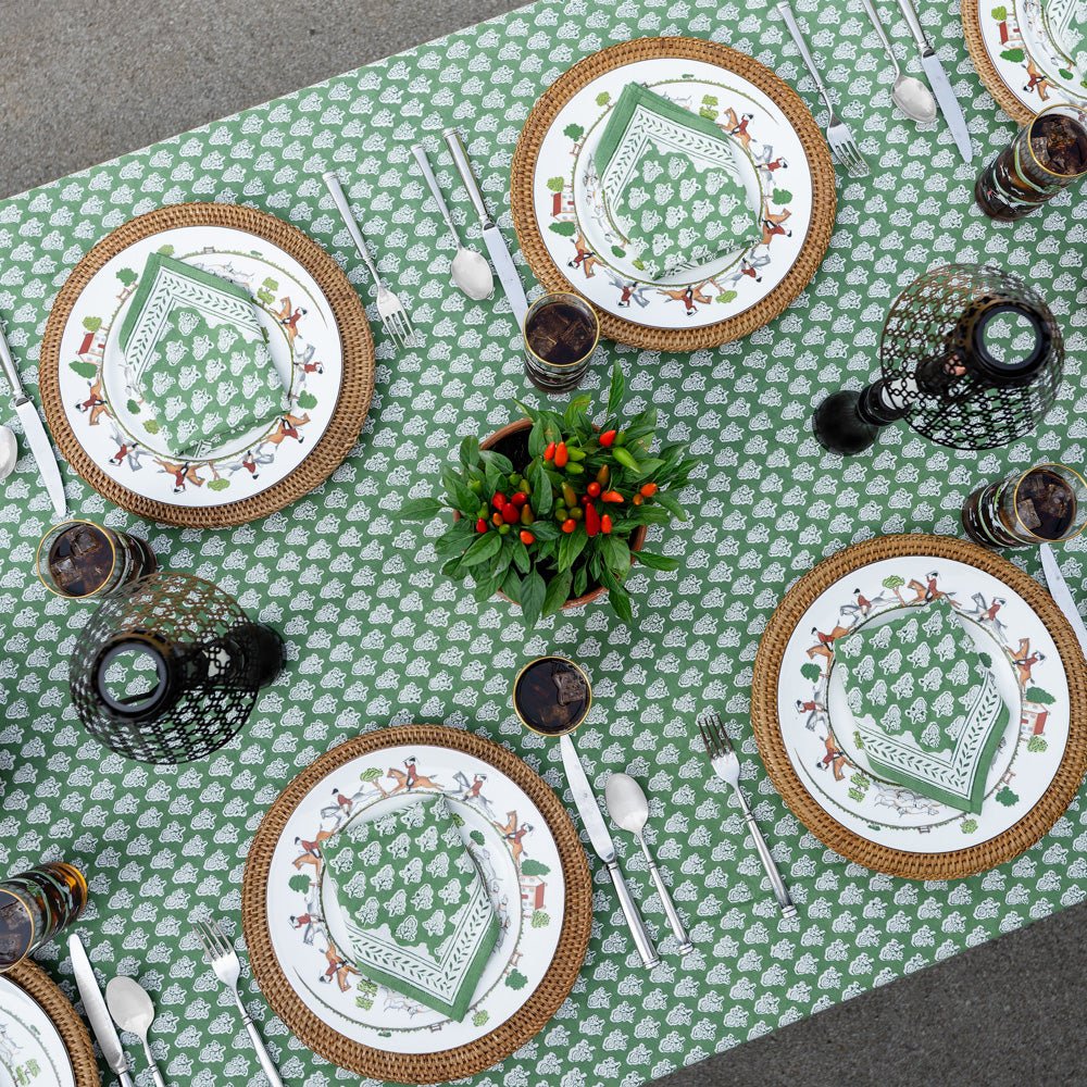 overhead view of table with pom buti green tablecloth and matching napkins on plates with wicker chargers