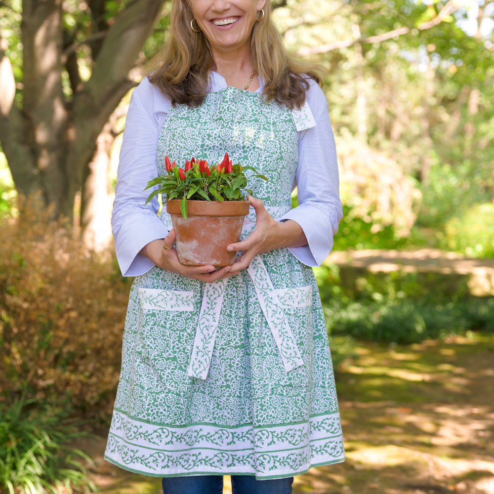 Model wearing tapestry green and white floral apron holding potted plant