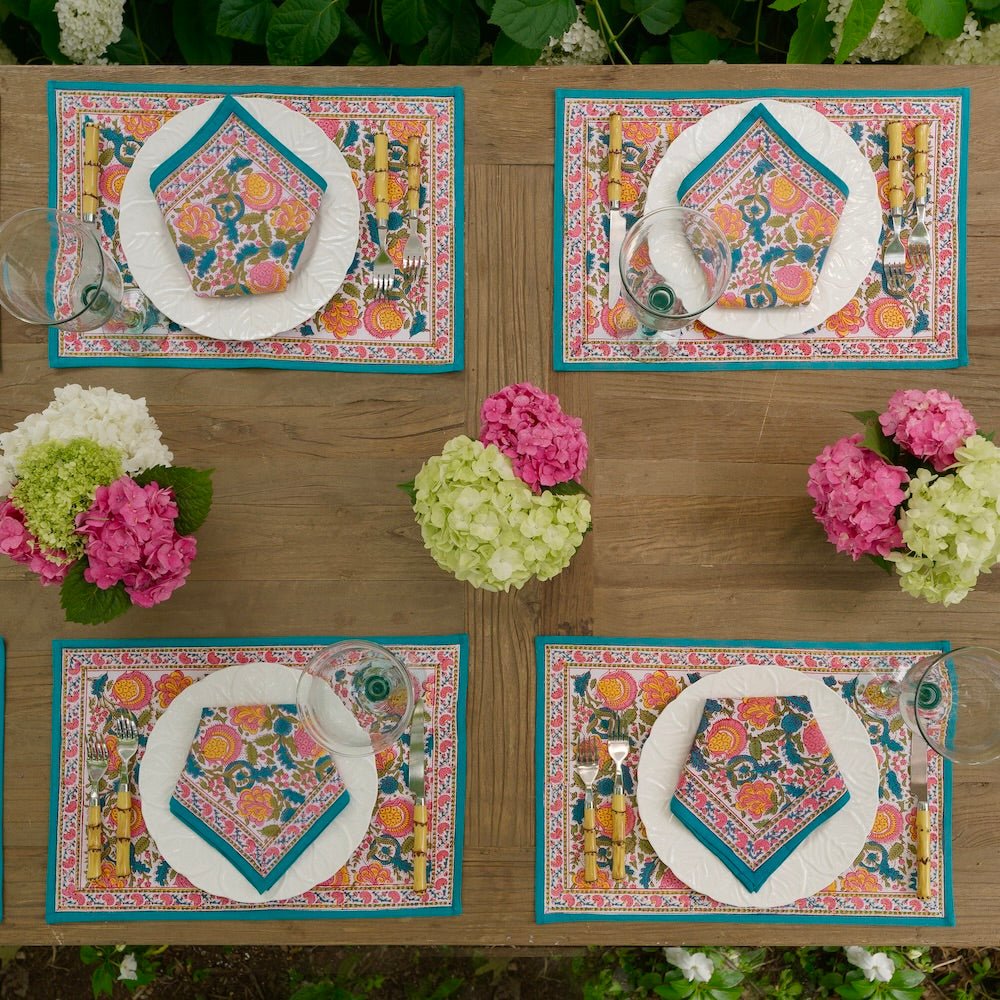overhead view of a table with 4 Jewel tone colored placemats with blossom design and matching napkins on white plates