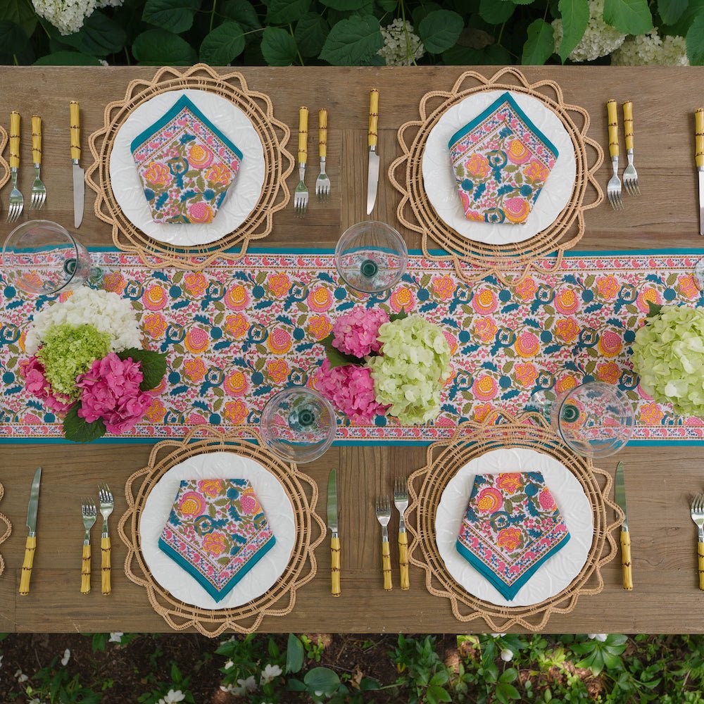 overhead view of a wooden table with Jewel tone colored table runner with blossom design and matching napkins on white plates