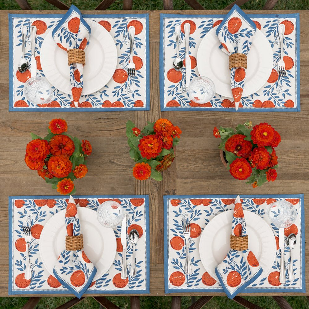 4 placemats with blue floral design and oranges on a wooden table with matching napkins and white plates