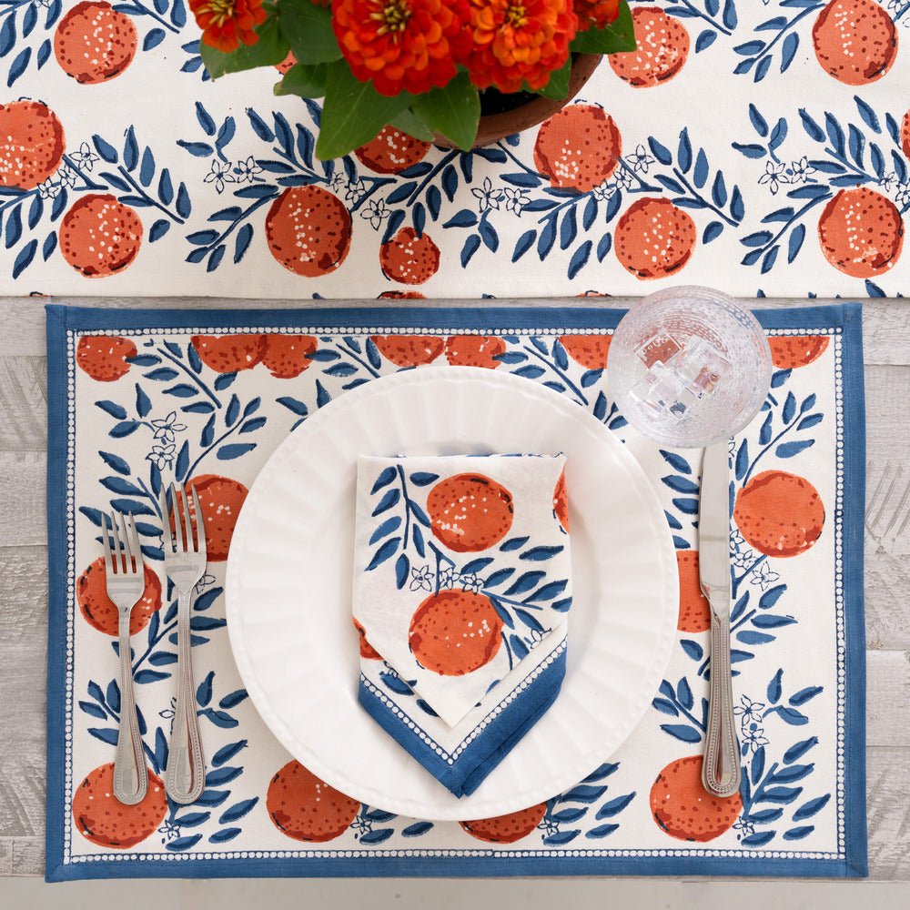 Placemat with blue floral design and oranges on a wooden table with matching napkin and white plate