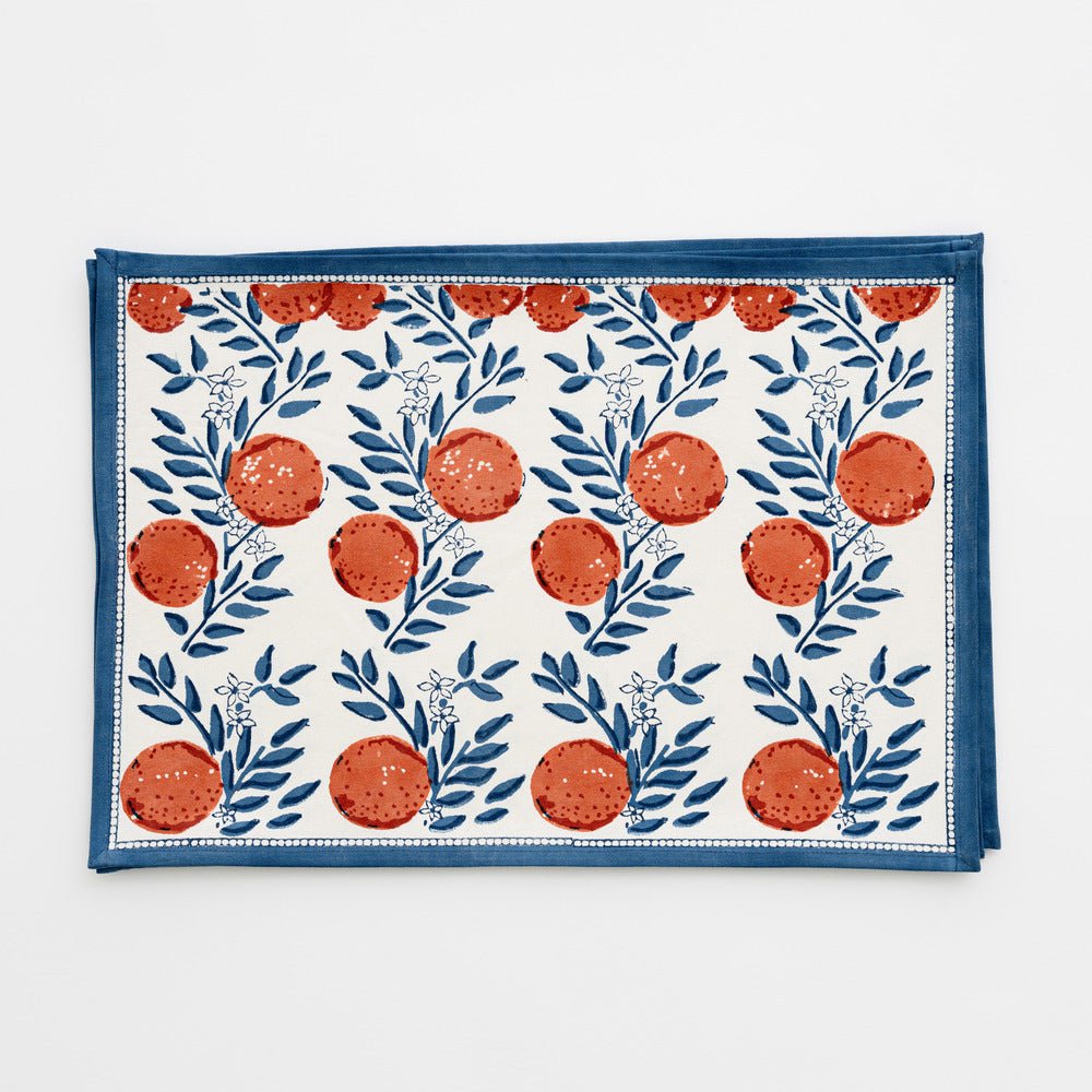 stack of placemats with blue floral design and oranges on a white background
