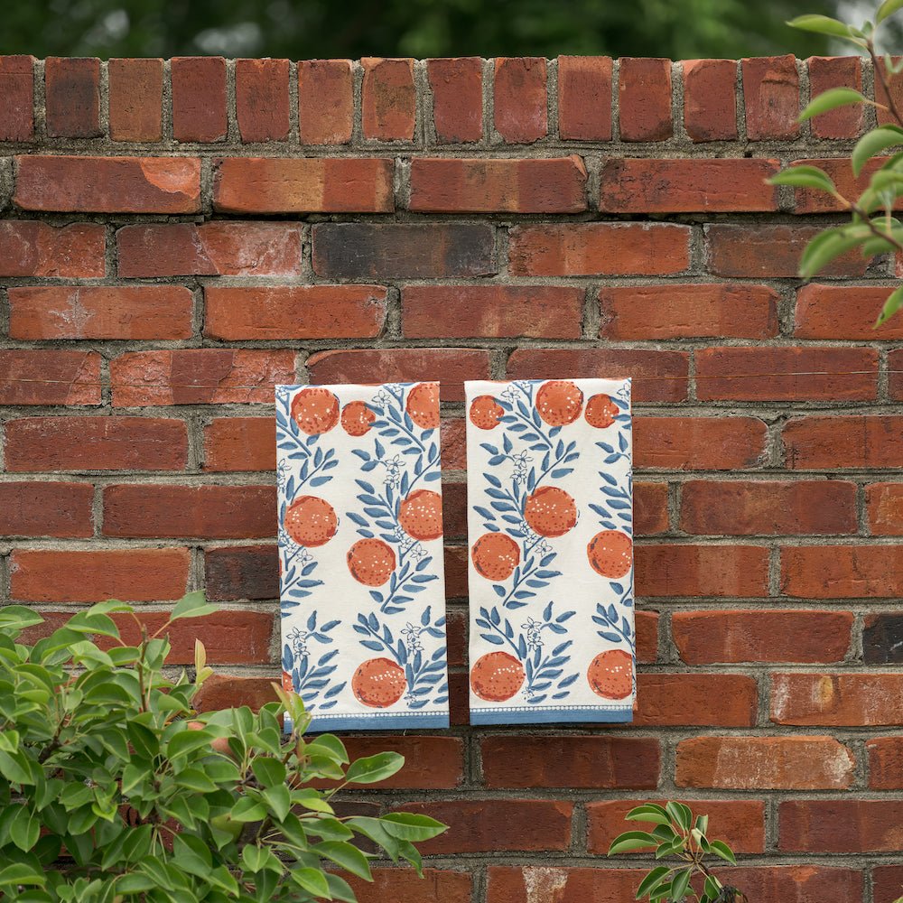 two tea towels printed with oranges and blue floral design hanging from brick wall