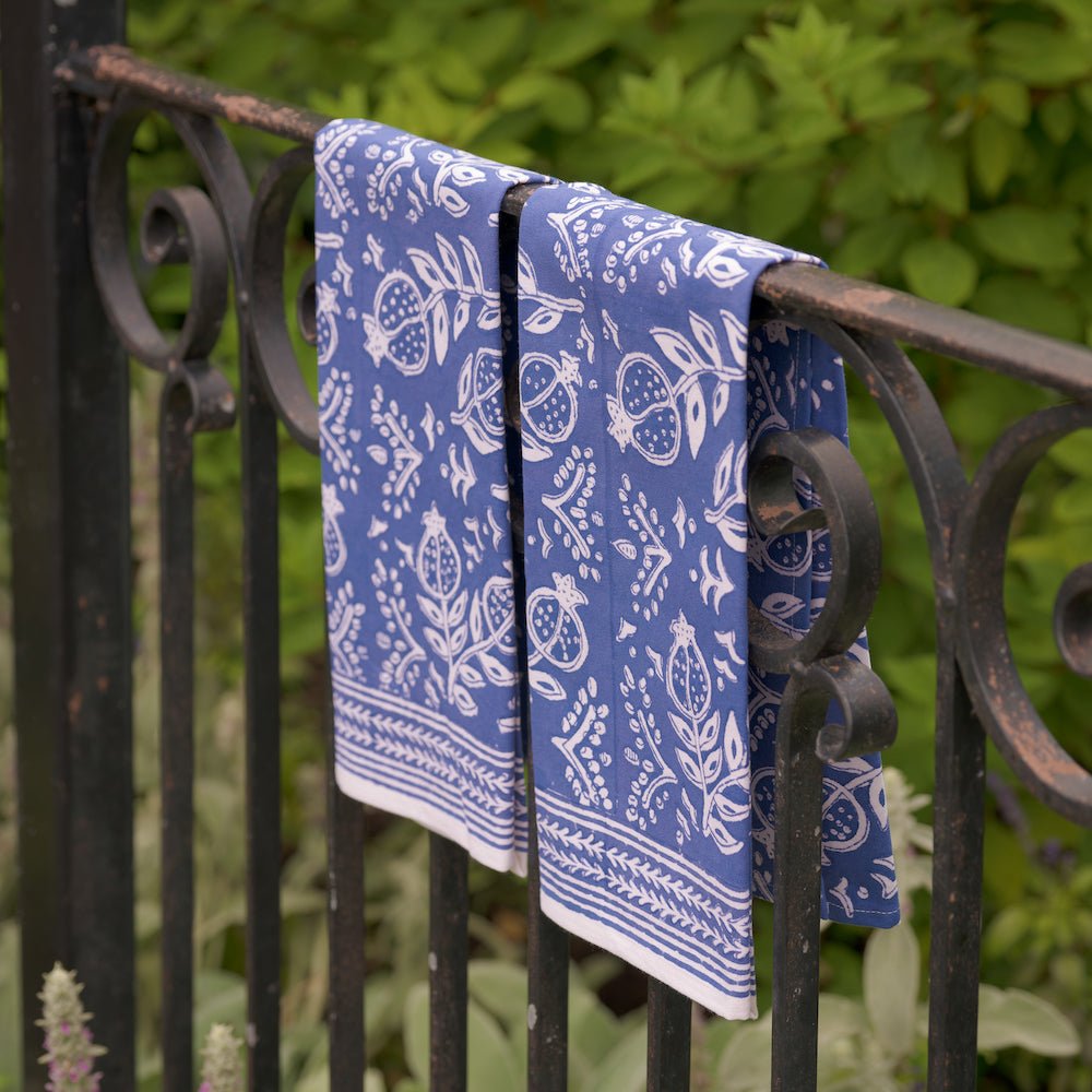 set of 2 pomegranate blue tea towels hanging over iron gate